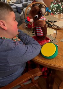 MJ sits at a table with a toy reindeer and a button switch.