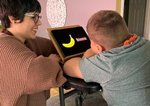 MJ looks at a picture of a banana placed on a velcro board in front of him. The word “Banana” is presented in letters beside the picture.