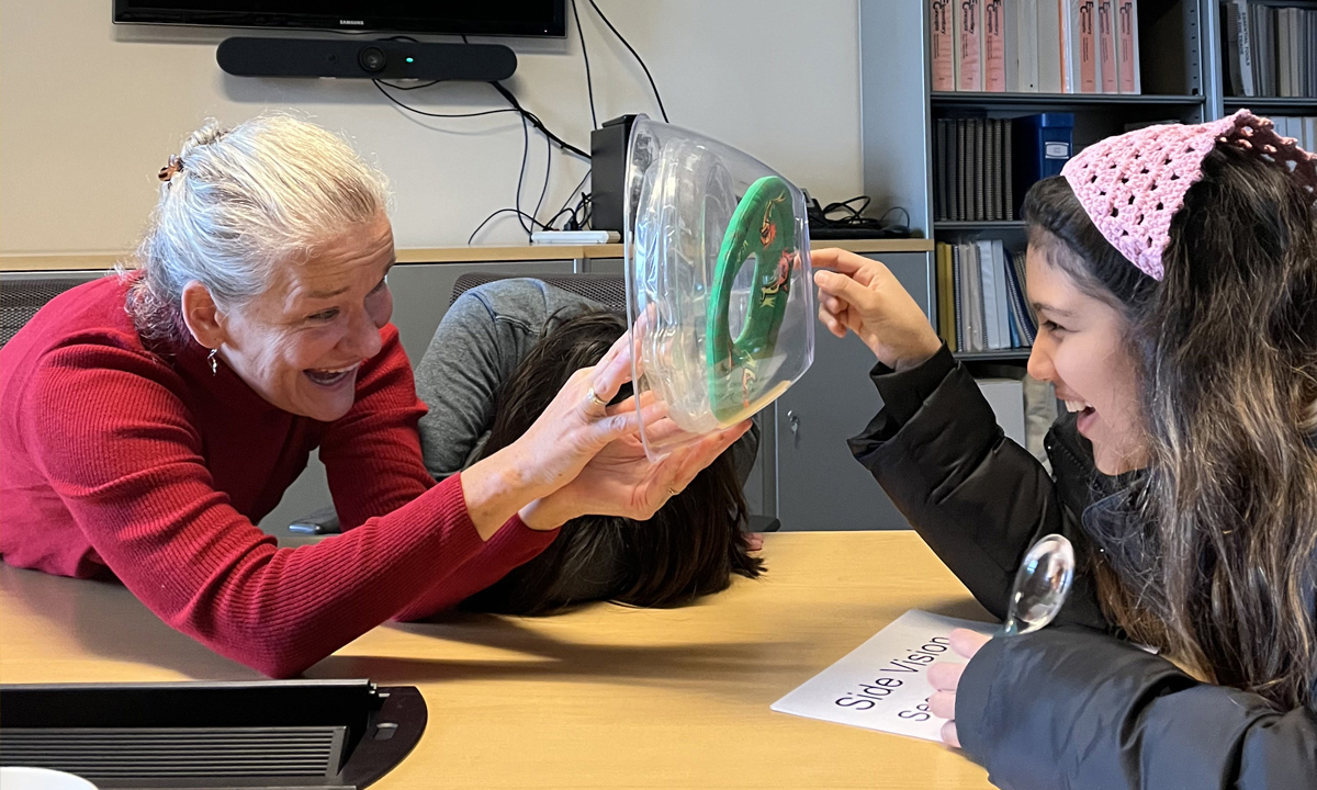 An adult and adolescent explore a clear bowl, frisbee disc ring representing the cornea, iris, and lens.