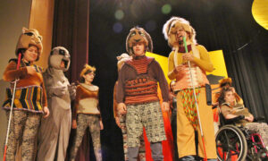 Six students dressed in costumes for Disney's The Lion King Jr. stand on an auditorium stage during a school production of the play.