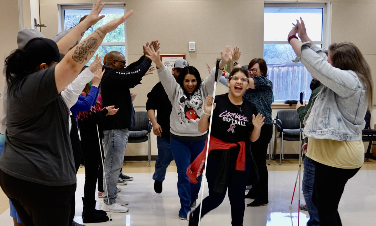 An adolescent and two caregivers dance down the center of two rows of adults and adolescents clapping, holding their arms up, and cheering.