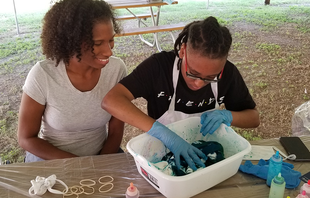 Student tie-dying outside with a staff member at a picnic table