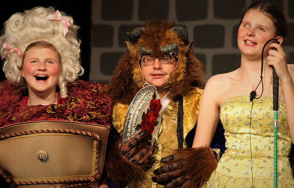 Three students on stage in costumes performing a play