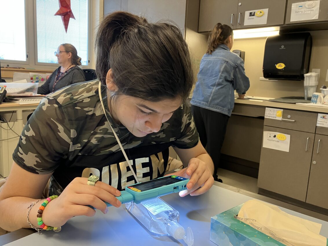 An adolescent uses a magnifier with illumination to read the small print on a sanitizer bottle.