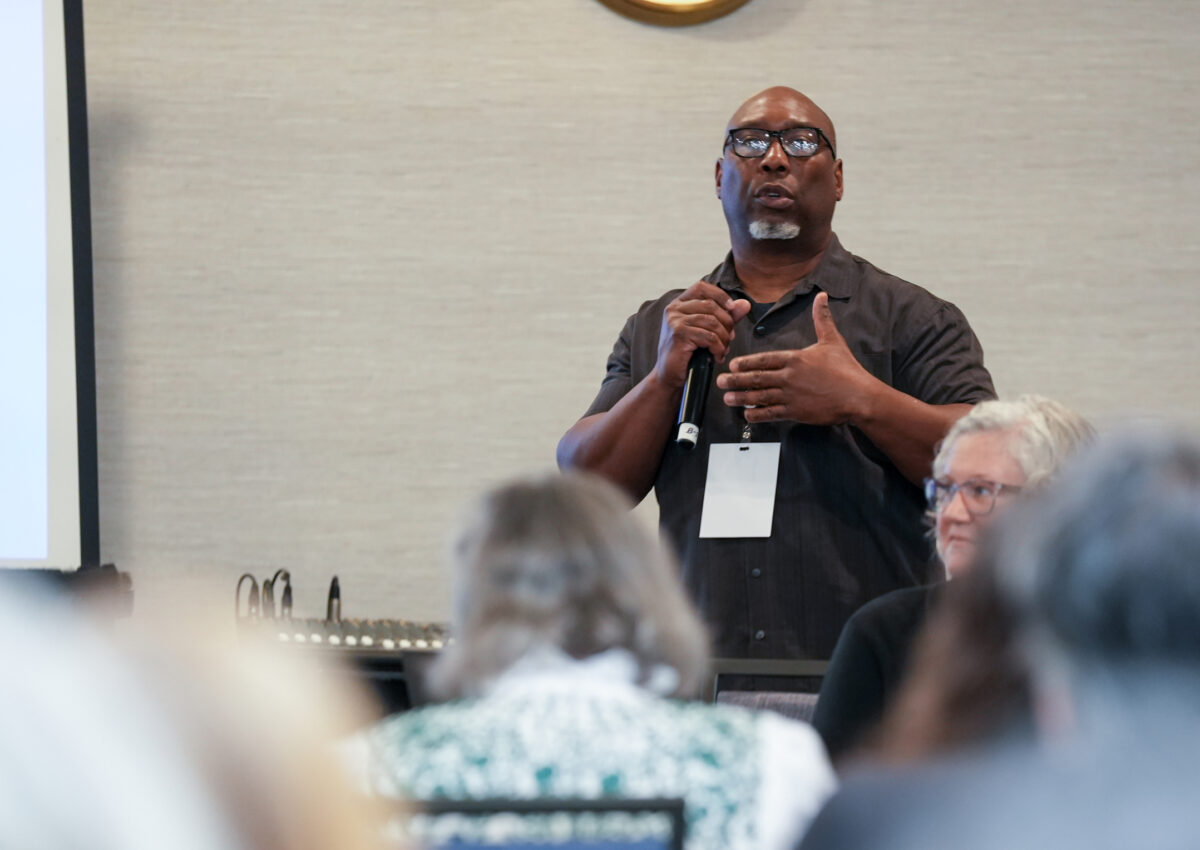 An adult speaks to a large group at a conference.