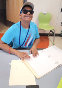 Un adolescente lee el texto en braille de una carpeta con tres aros que está abierta.