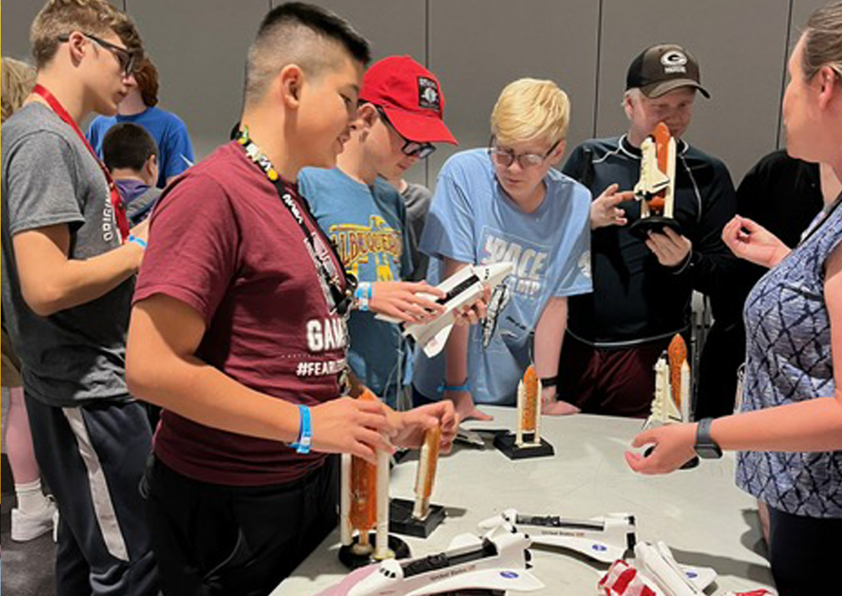 Un grupo de campistas exploran las maquetas del transbordador espacial en un aula.