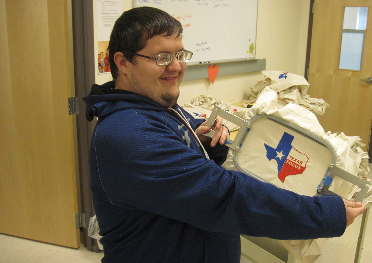 An adolescent shows off a bag he embroidered for a Texas Focus Conference with the state of Texas on the tote.