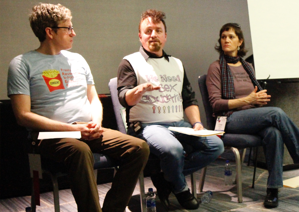 Three adults sit on a panel wearing shirts with messages about sexuality education.