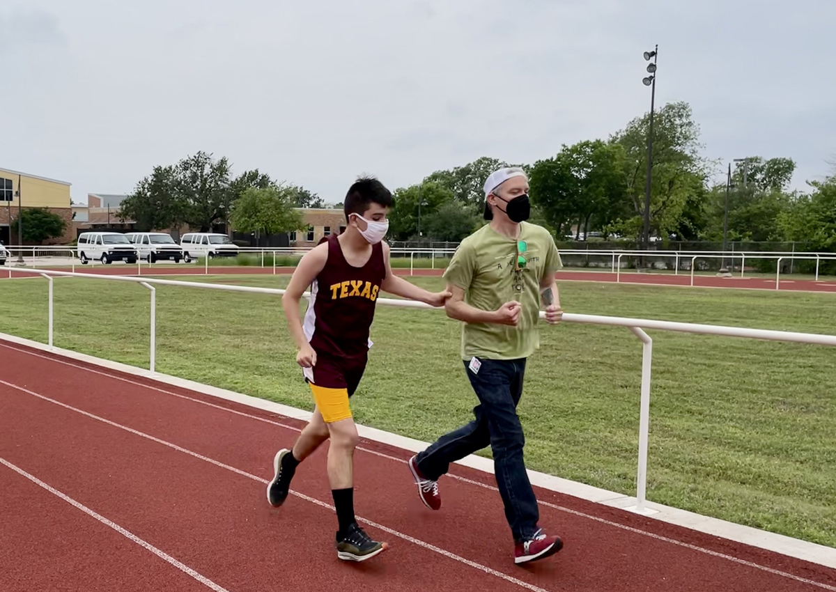 Staff guide running with student in the 200 meter dash.