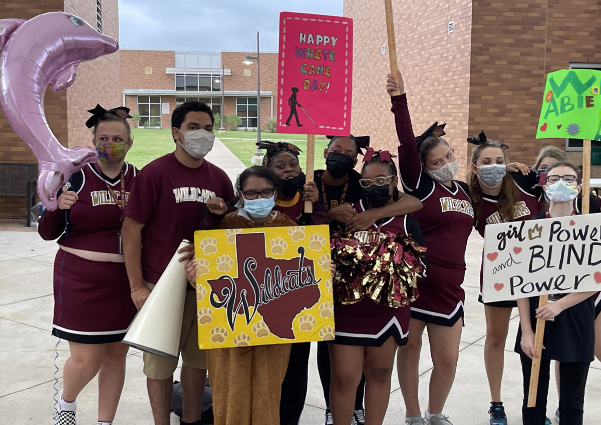 Cheerleaders hold White cane day signs., poms and balloons.