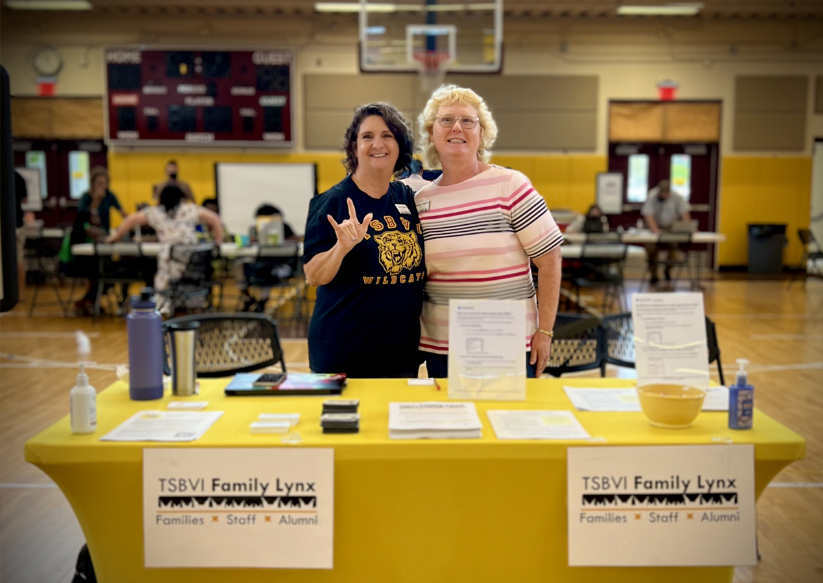 Two adults stand in a side hug, one holds up 