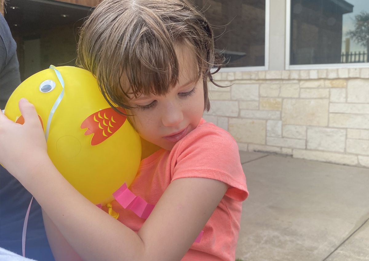 An adolescent hugs a yellow balloon with chicken stickers on it.
