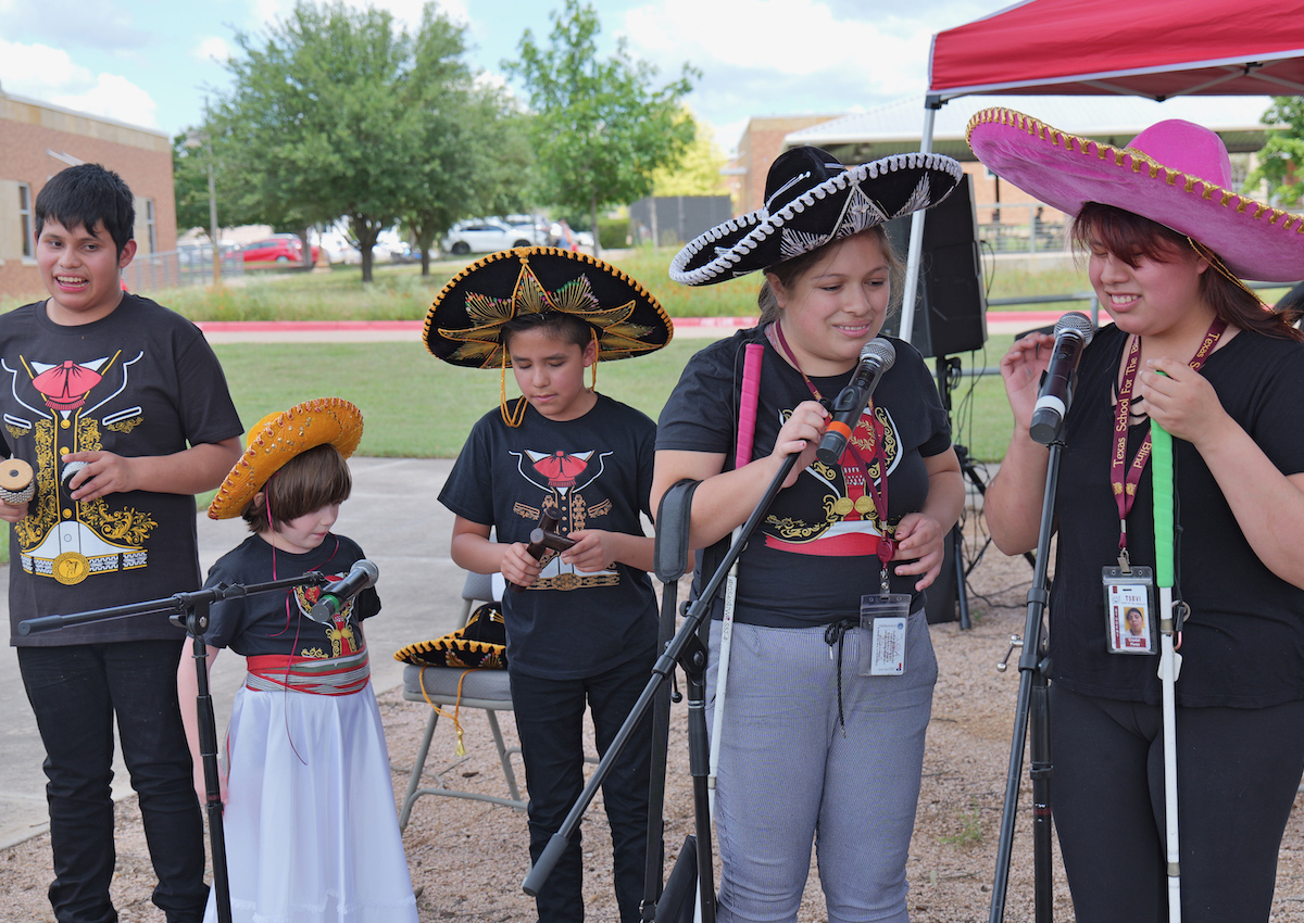 Five adolescents perform outdoors in matching mariachi t-shirts and sombreros.