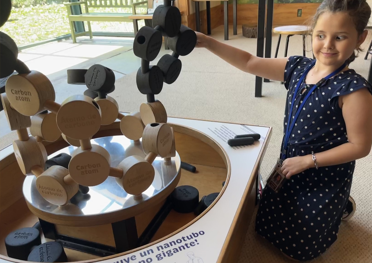 An adolescent holds up a life-size model of carbon atoms linked together by nanotubes at a Science Center.