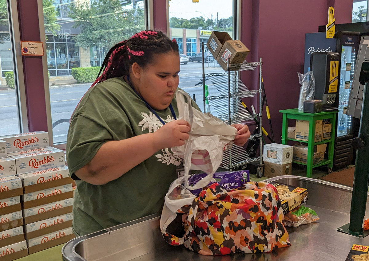 An adolescent bags groceries in a grocery store.