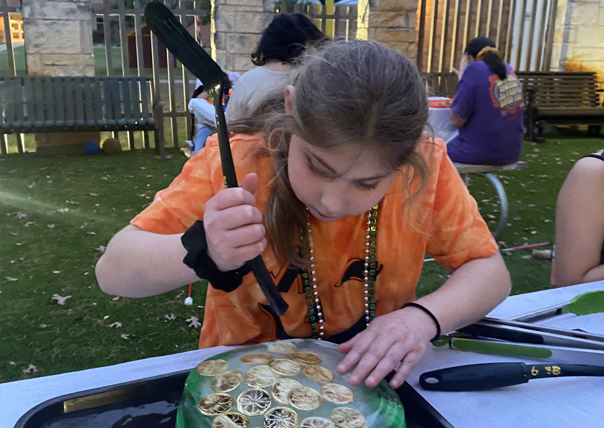 An adolescent smashes objects related to St. Patrick's Day frozen in ice in a container at a picnic table outdoors in the evening.