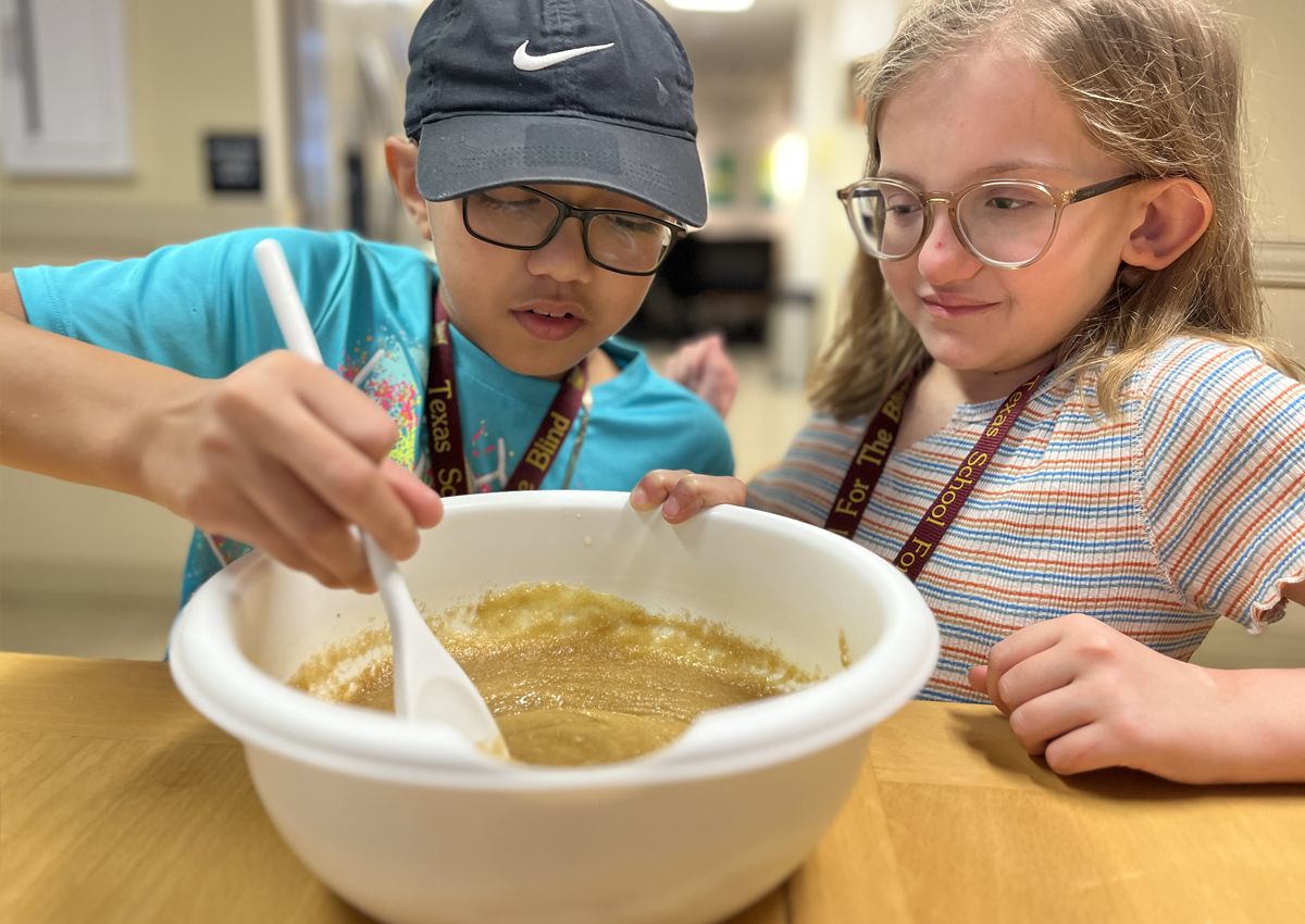 Two adolescents mix cookie batter in a residential dining room.