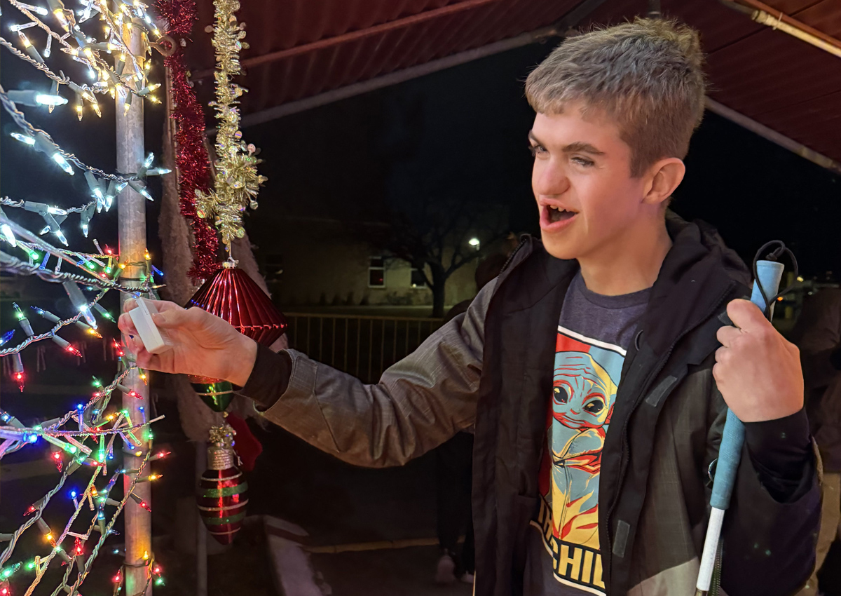 An adolescent smiles while inside a carport on an outdoor track decorated with hundreds of Christmas lights.