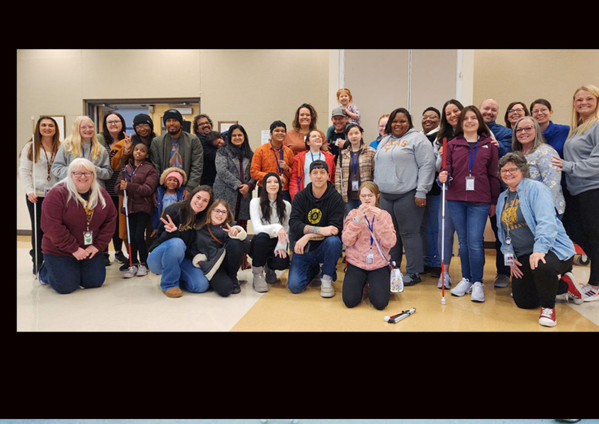 A large group of adults and adolescents, some with white canes, pose in a conference room.