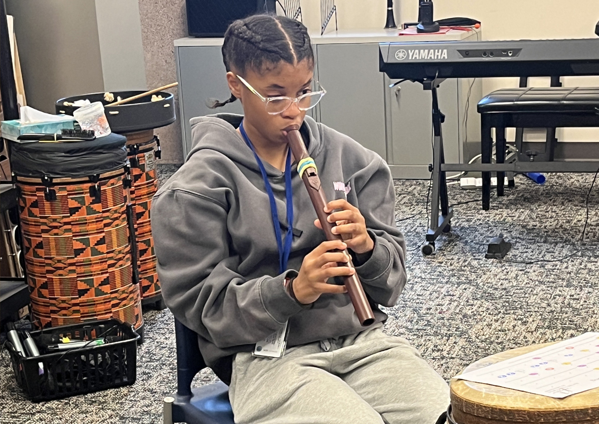 An adolescent plays a Native American Flute while seated in a music room.