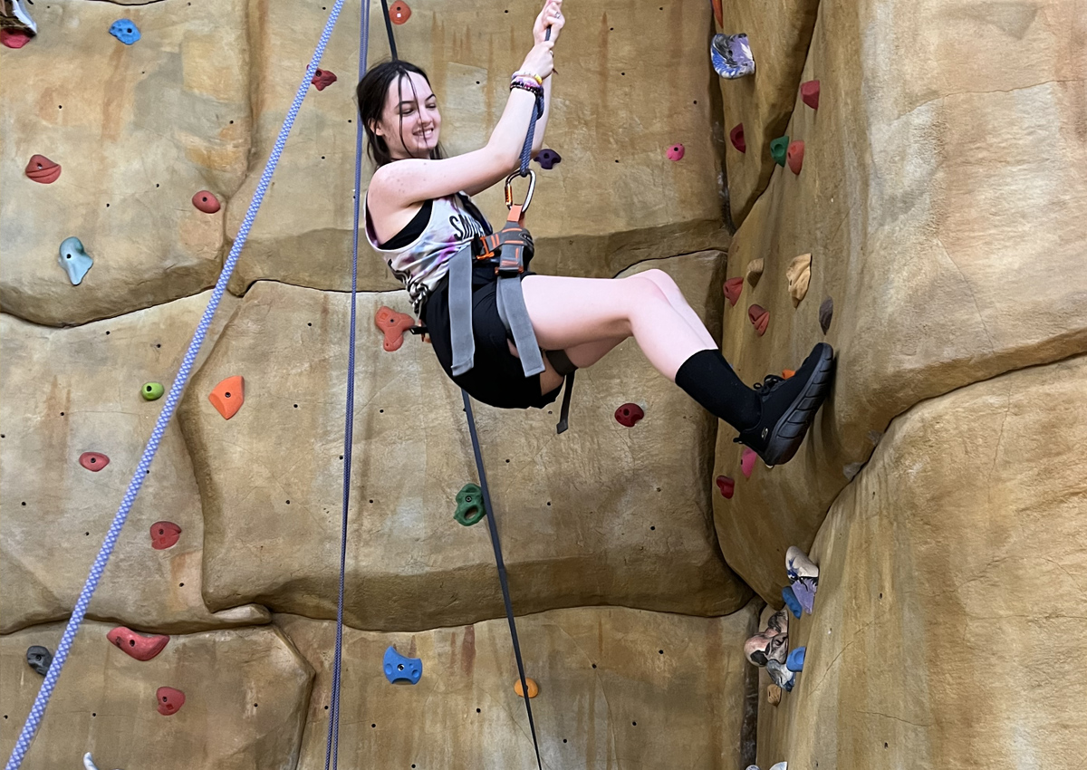 An adolescent climbs an indoor rock wall.