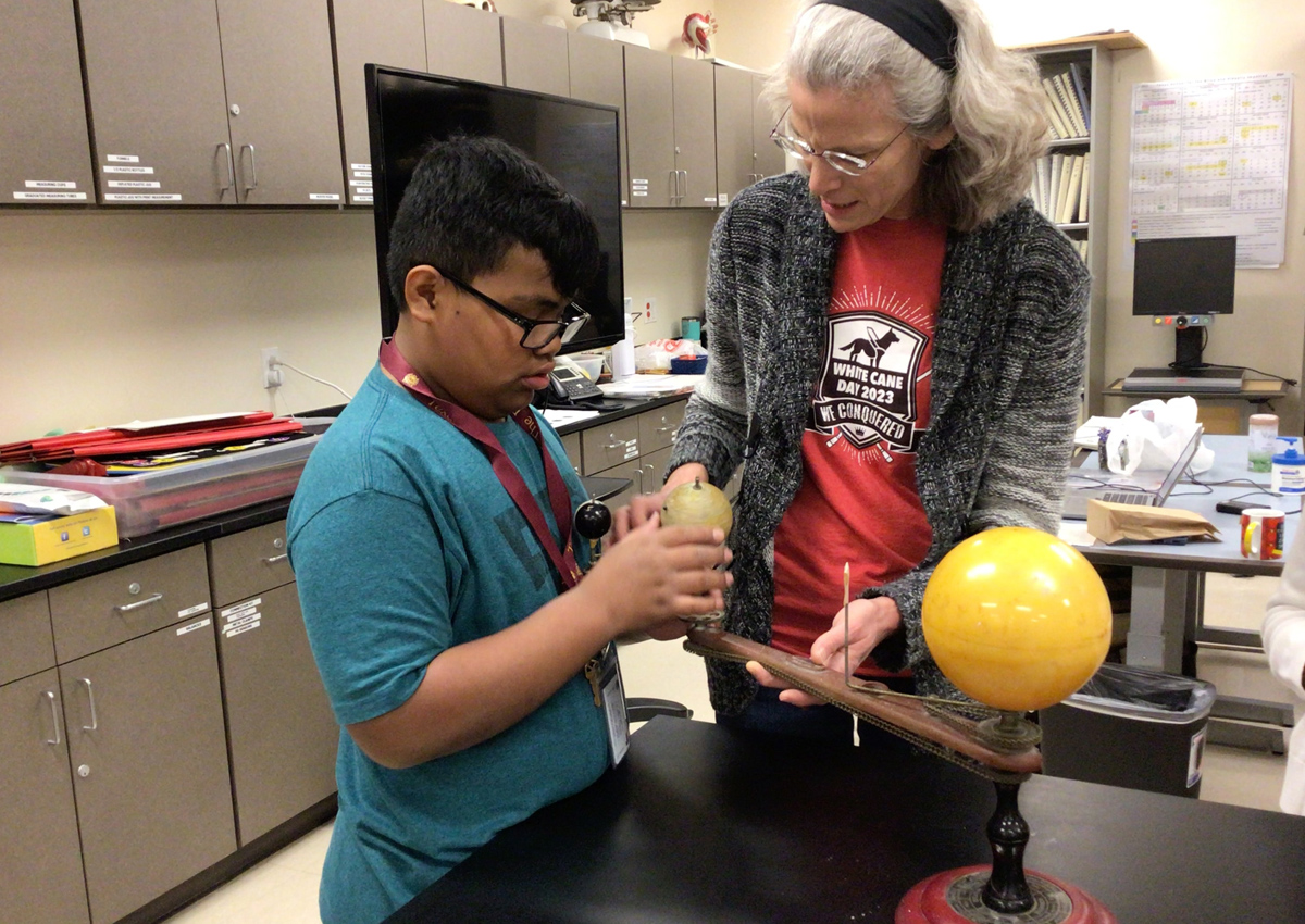 An adult and adolescent explore a model of the Sun- Earth- Moon System in a science lab.