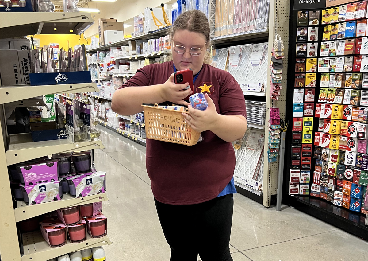 An adolescent in a grocery store holds a basket that says 