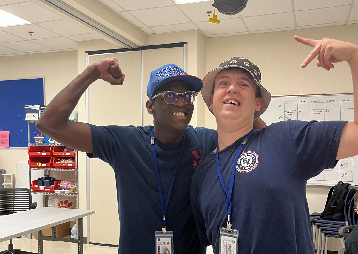 Two adolescents flex their muscles in a work room.