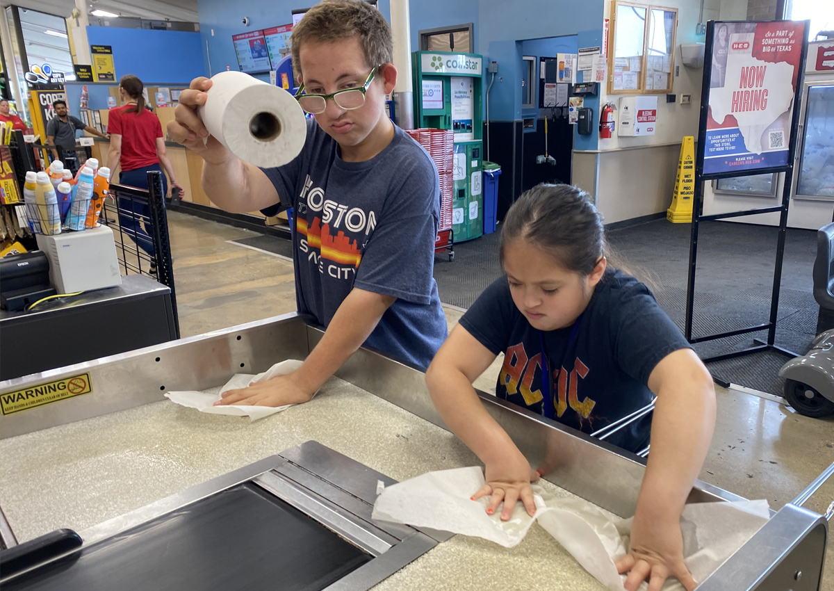 Two adolescents clean the bagging area at the HEB.