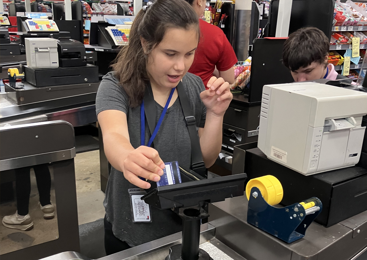 An adolescent uses a card to pay at a grocery store.