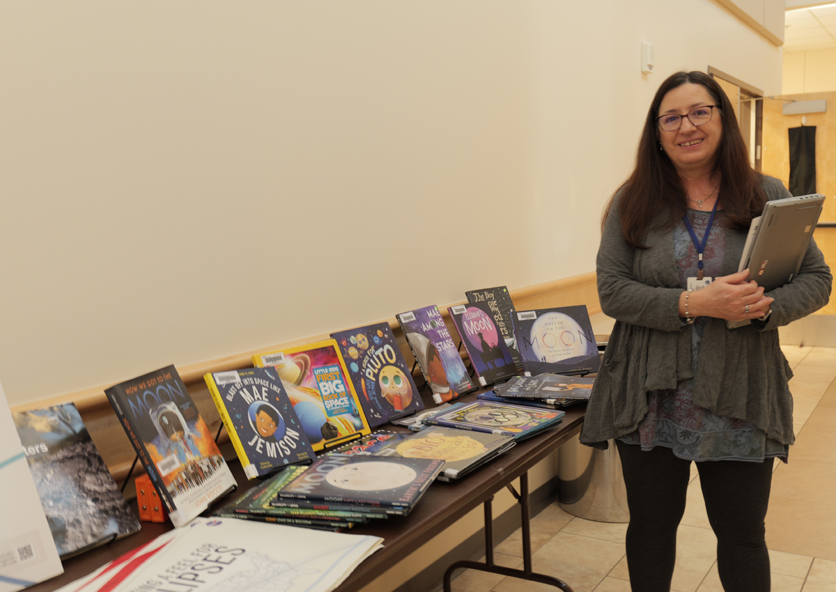 An adult stands in a hallway next to a display of astronomy and science books for kids.