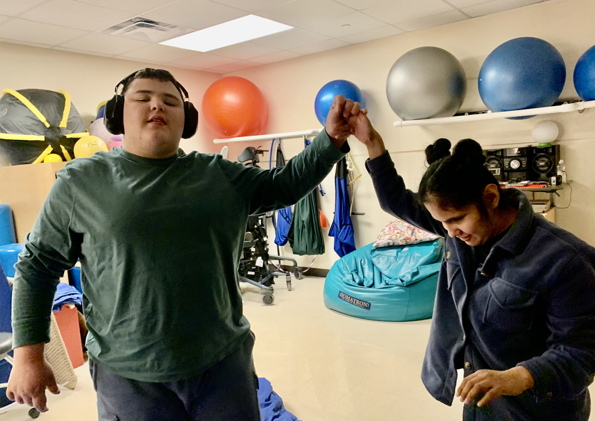 Two adolescents in a sensory movement room hold hands and lift their arms up in the air.
