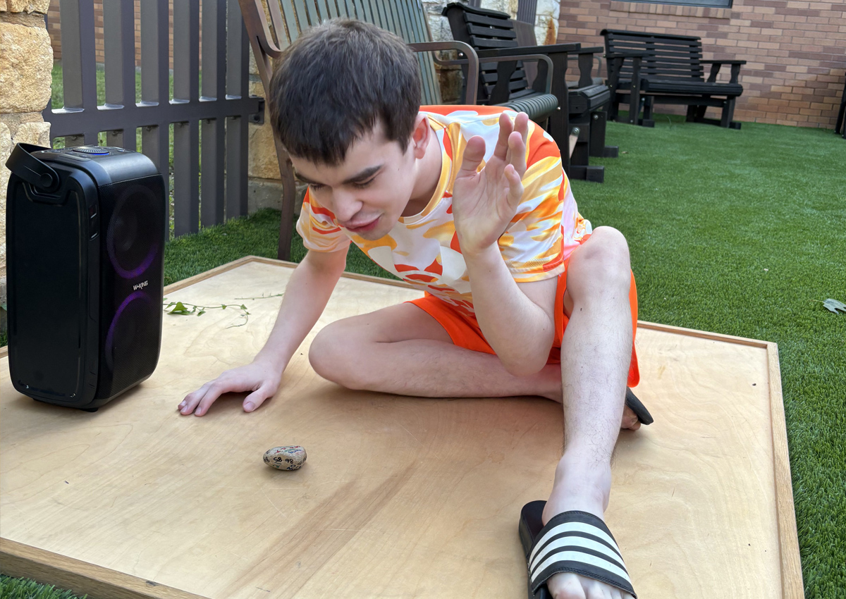 An adolescent on a resonance board with a rock and a speaker.