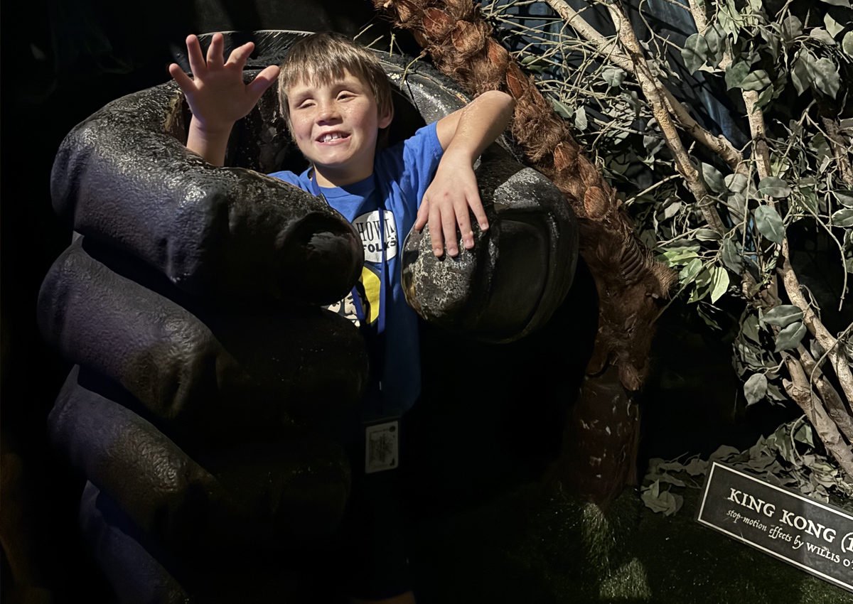An elementary student smiles in the large grip of a King Kong paw.