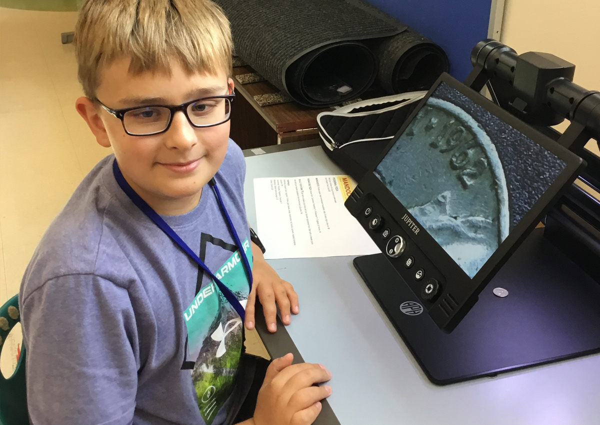 An adolescent uses a Jupiter Portable Magnifier to magnify a coin.