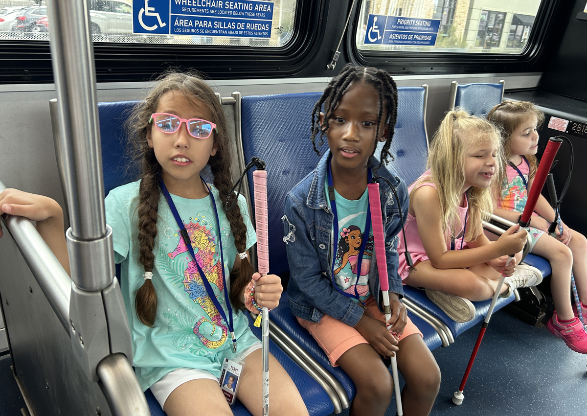 Four elementary students with white canes ride the city bus.
