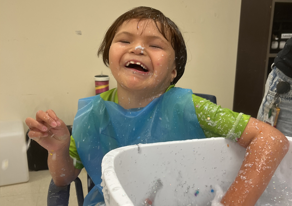 An elementary student reaches his hand into a bucket with liquid paper pulp.