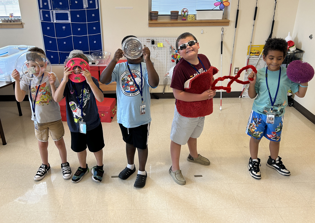 Five elementary students in a classroom hold household items they used to represent parts of the eye.