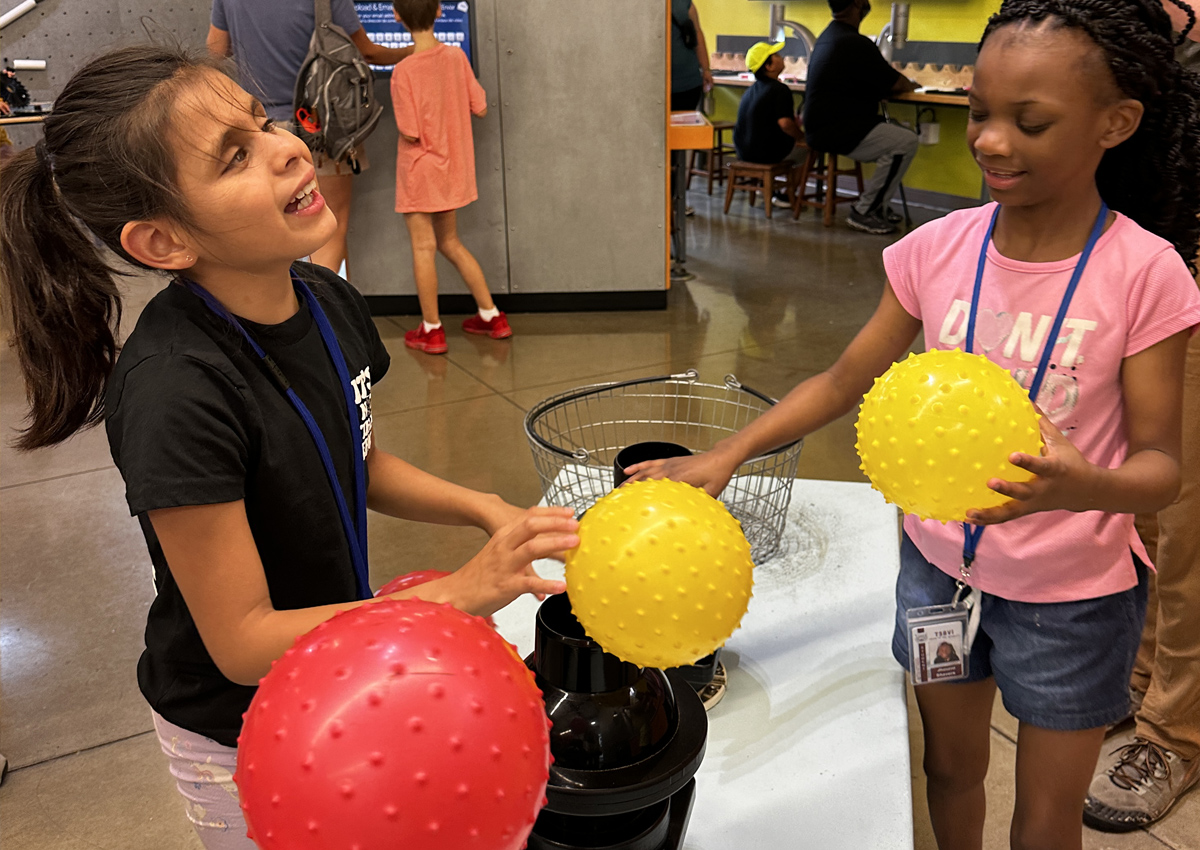 Two adolescents balance bumpy textured balls over air machines that enable the balls to float.