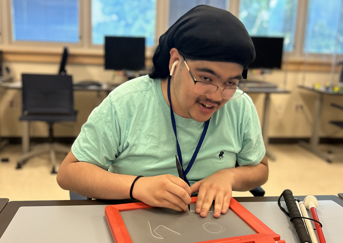 An adolescent makes a tactile drawing on a tactile drawing board.