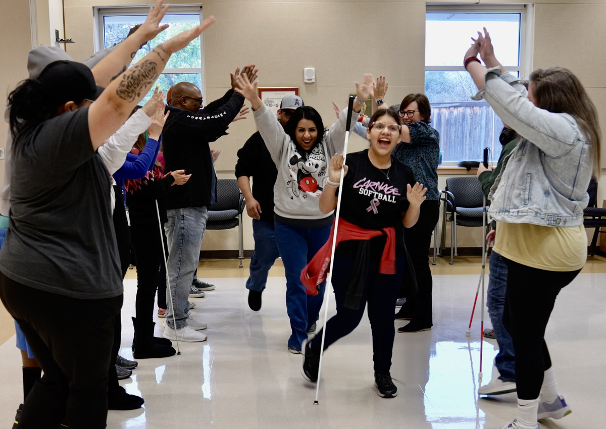 An adolescent and two caregivers dance down the center of two rows of adults and adolescents clapping, holding their arms up, and cheering.