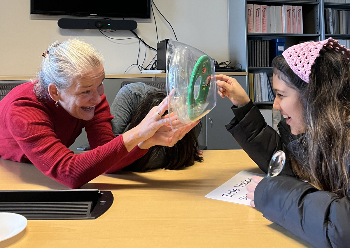 An adult and adolescent explore a clear bowl, frisbee disc ring representing the cornea, iris, and lens.