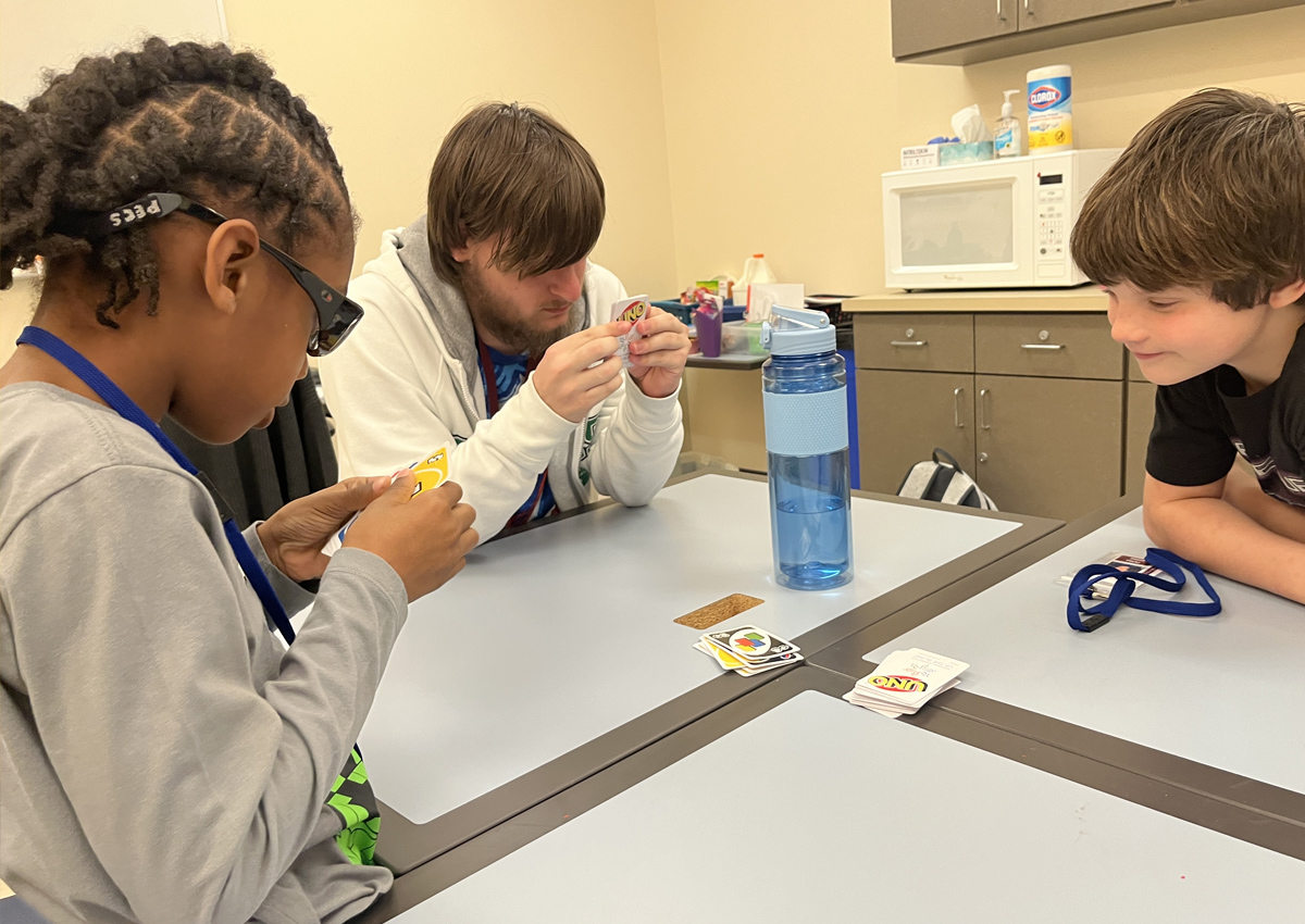 Two elementary students and an adolescent play UNO.