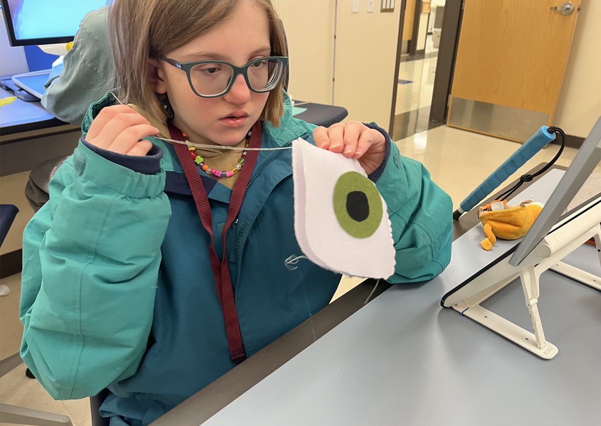 An adolescent sews a felt eye pillow.
