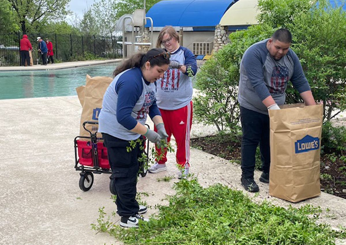 Three adolescents wearing Lion's Club Work Day shirts weed gardens.