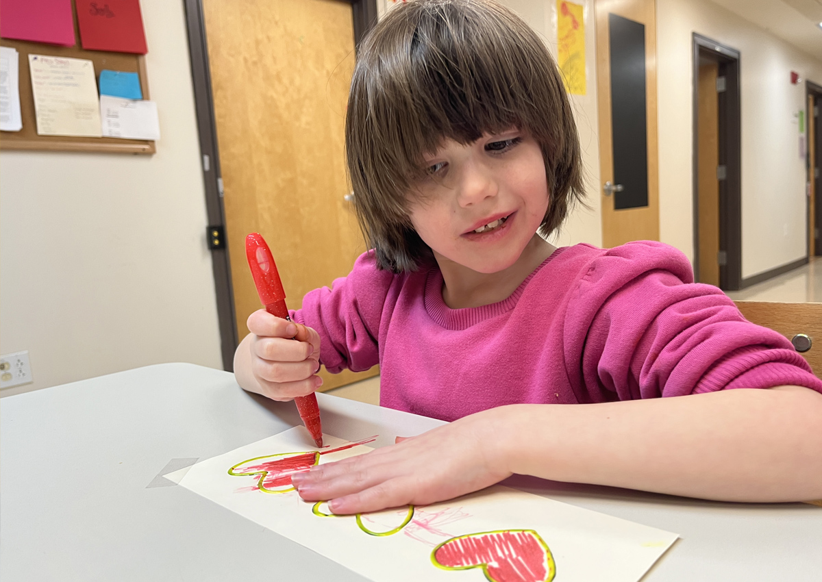 An adolescent uses a marker to color in hearts made with raised lines.