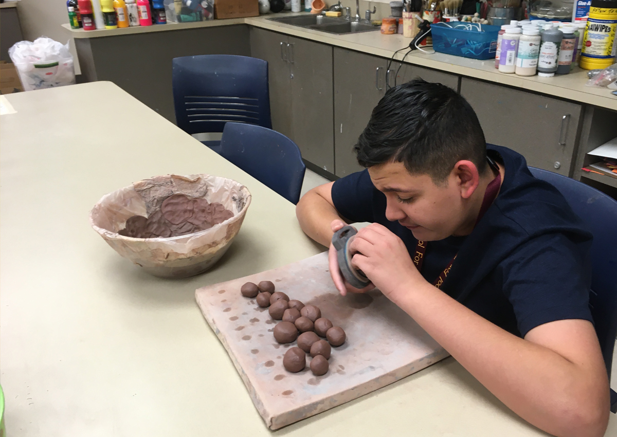 An adolescent rolls balls of clay and then pushes them into a bowl mold to make a ceramic bowl.