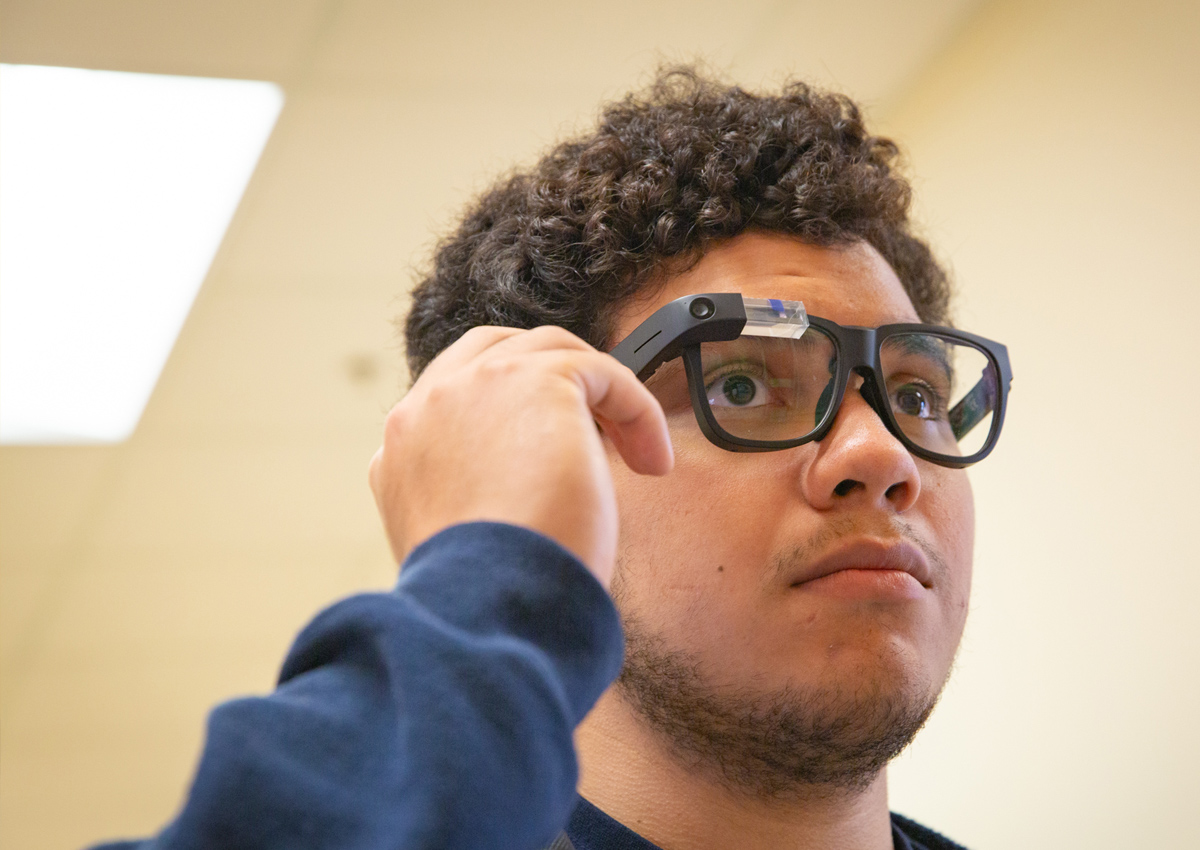 An adolescent uses his right hand to touch the right side of the Envision glasses.