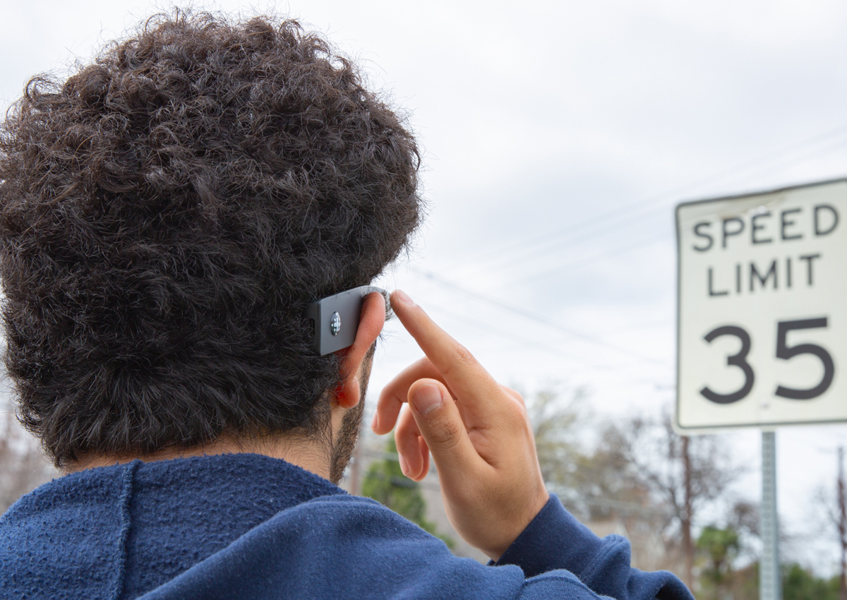 An adolescent uses the index finger of his right hand to tap the side of his Envision glasses.